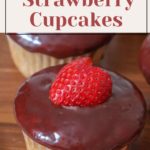 A delectable strawberry cupcake, topped with a rich chocolate glaze and garnished with a halved strawberry, sits invitingly on the wooden surface.