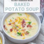 A bowl of baked potato soup, luxuriously topped with cheese, crispy bacon, and fresh chives rests on a cloth napkin. Text above promises: "The Best Homemade Baked Potato Soup Recipe.