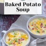 Two bowls of creamy baked potato soup sit invitingly on a cloth, topped with shredded cheese, crispy bacon bits, and fresh green onions. A pot in the background suggests there's plenty more to enjoy.