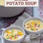 Two bowls of creamy baked potato soup garnished with cheese and crispy bacon sit invitingly on a rustic wooden table.