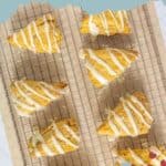 A cooling rack with eight triangular, glazed pumpkin scones sits on a light blue background. The text reads "coffeehouse favorite PUMPKIN SCONES" and "stetted.com" with a small berry design.