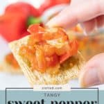 Close-up of a hand holding a cracker topped with sweet pepper relish. The background is slightly blurred, showcasing more sweet pepper relish and vibrant peppers. Text at the bottom reads, "Tangy Sweet Pepper Relish".