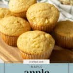 A wooden board with six delicious apple muffins. A basket of apples is visible in the background. The text on the image reads: "stetted.com MAPLE apple MUFFINS.