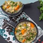 Two bowls of hearty chicken wild rice soup garnished with fresh herbs sit on a patterned cloth, with sprigs of parsley nearby.