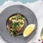 Plate with kale quinoa stuffed squash and a lemon wedge, placed on a grey dish. Text at the top reads, "STUFFED SQUASH," and website "stetted.com" is at the bottom.