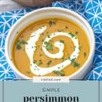 A bowl of persimmon sweet potato soup garnished with a swirl of cream and chopped herbs, set on a blue patterned tablecloth alongside a plate of bread.