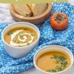 Two bowls of persimmon sweet potato soup garnished with cream and parsley, accompanied by a whole persimmon and bread slices in the background.