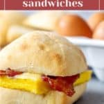 A close-up of a bacon and gouda breakfast sandwich in a bread roll. In the background, there is a carton of eggs. The text "Bacon Gouda Breakfast Sandwiches" is at the top, reminiscent of Starbucks breakfast sandwiches.