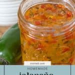 A jar of homemade jalapeño jelly is displayed in front of fresh jalapeños and a bowl of cereal, with a charming tag that reads "stetted.com.