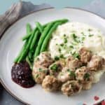 A plate with Swedish meatballs topped with rich gravy, creamy mashed potatoes, crisp green beans, and a side of tangy lingonberry jam. Text reads "homemade Swedish meatballs" and "stetted.com.