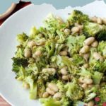 A bowl of vibrant broccoli white bean salad sits on a rustic wooden table, featuring crisp broccoli florets and tender white beans mixed to perfection.