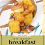 A spoonful of breakfast potatoes, roasted to perfection with savory herbs and crispy pieces, rests invitingly on a decorative plate.