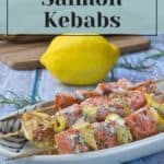         Plate of grilled salmon kebabs with vegetables, garnished with herbs, on a white dish. A whole lemon is in the background. Text reads: 'How to Make the Best Salmon Kebabs.'