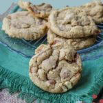 A plate of delectable salted caramel cashew cookies sits on a green cloth, with one tantalizing cookie taking the spotlight in the foreground.