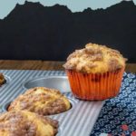 Maple walnut muffins in a baking tray, with one delicious muffin resting on a blue patterned napkin.