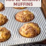 Baked maple walnut muffins in a striped muffin pan resting on a table with a blue patterned cloth.