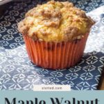 A maple walnut muffin sits elegantly on a blue patterned cloth, complemented by a tray of its delicious counterparts in the background. Delectable "maple walnut muffins" text graces the image, inviting you to visit stetted.com for more.