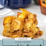 Close-up of a serving of slow cooker pumpkin French toast on a white plate, with a blue slow cooker and a bottle in the background. Text at the bottom reads "Slow Cooker Pumpkin French Toast".