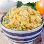 A vibrant bowl of persimmon salsa with fresh herbs rests on a rustic wooden surface, accompanied by the subtle hint of an orange peeking from the background.