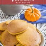 A white bowl filled with delicious pumpkin pancakes is set on a table, exuding a warm autumn vibe. A small pumpkin and a neatly folded blue napkin are placed in the background. Text overlay reads "Pumpkin Pancakes Easy Recipe.