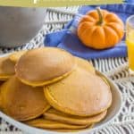 A plate of pumpkin pancakes is set on a table with a small pumpkin, a glass of orange juice, and a blue napkin. The text reads: "Pumpkin pancakes - the spiced fall favorite at stetted.com.