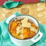 A small white dish brimming with delectable pumpkin bread pudding rests elegantly on a teal cloth.