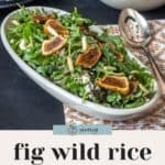 A bowl of fig wild rice salad on a table, garnished with fresh greens and sliced figs. A serving spoon rests beside the bowl. In the background, there's a smaller bowl containing whole figs.