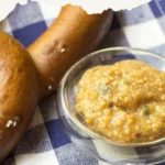 A small dish of flavorful lemon sage mustard sits next to pretzels on a blue and white checkered cloth, ready to elevate your snack experience.