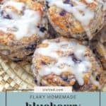 A close-up of a basket filled with flaky, homemade blueberry biscuits drizzled with icing. The text reads: “stetted.com Flaky Homemade Blueberry Biscuits.”