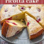 A delectable raspberry ricotta cake, dusted with powdered sugar, sits elegantly on a round cake stand, enticing with its few perfectly sliced pieces.