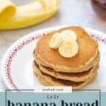 A stack of delectable banana bread pancakes topped with fresh banana slices sits on a plate. In the background, a peeled banana and a cup of syrup await to enhance this delightful breakfast treat.