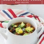 A bowl of sweet potato black bean chili garnished with avocado and herbs is placed on a striped cloth. The text reads “sweet potato black bean chili – easy recipe.”