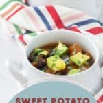 Two white bowls of sweet potato black bean chili topped with avocado and herbs are placed on a white surface, accompanied by a multicolored striped cloth. Text at the bottom reads "Sweet Potato Black Bean Chili." This hearty dish is both visually appealing and deliciously satisfying.