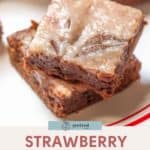 A tempting close-up of two strawberry cheesecake swirl brownies stacked on a plate highlights their marbled top layer, embodying a delightful fusion of rich chocolate and creamy strawberry cheesecake swirls.