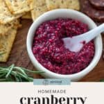 A bowl of homemade cranberry mustard with a spoon, surrounded by crackers and slices of sausage. Text reads: "Homemade cranberry mustard perfect for gifting this season.