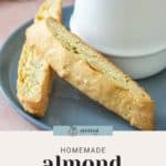 Plate with two almond biscotti pieces next to a white mug of coffee. The text "Homemade almond biscotti" is at the bottom, highlighting the delightful treat.