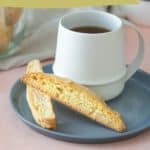 A white cup of coffee or tea sits on a grey plate with two pieces of almond biscotti. Text at the top reads "almond biscotti"; text at the bottom reads "perfect for coffee or tea" and the website www.stetted.com. Indulge in almond biscotti bliss.