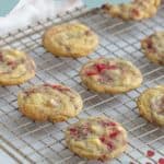 Raspberry white chocolate cookies cooling on a wire rack with text at the top reading "raspberry white chocolate cookies." Below, a website link awaits your visit for the delicious recipe.