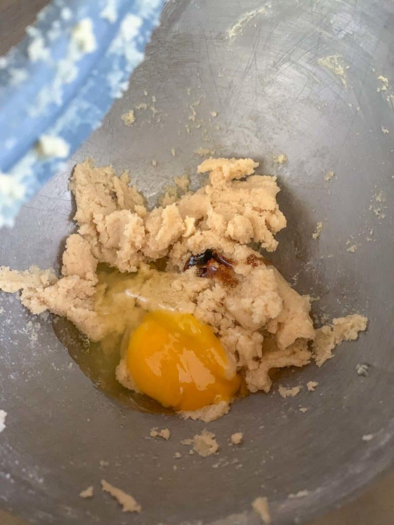 egg and vanilla being added to sugar and butter in mixing bowl