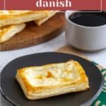 A cheese danish on a black plate next to a cup of coffee, with more cheese danishes on a wooden tray in the background. Text overlay reads "Easy Homemade Cheese Danish.