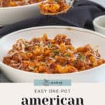 Two bowls of savory American goulash are topped with melted cheese and fresh herbs. A fork lifts a delicious bite, capturing the perfect blend of flavors.