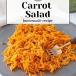 A plate of vibrant carrot salad graces a gray dish, accompanied by a fork. In the background, a small jar of green dressing awaits to enhance the fresh flavors.