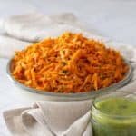 A plate of vibrant carrot salad sits on a cloth, accompanied by a jar of green dressing. Text reads: "Carrot Salad - an easy & delicious recipe.