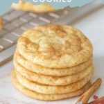 A tempting stack of homemade snickerdoodle cookies graces the countertop, with a cooling rack and aromatic cinnamon sticks in the background.