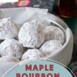 A bowl of powdered sugar-coated bourbon balls on a table with bottles in the background. The image has text that reads, "Maple Bourbon Balls.