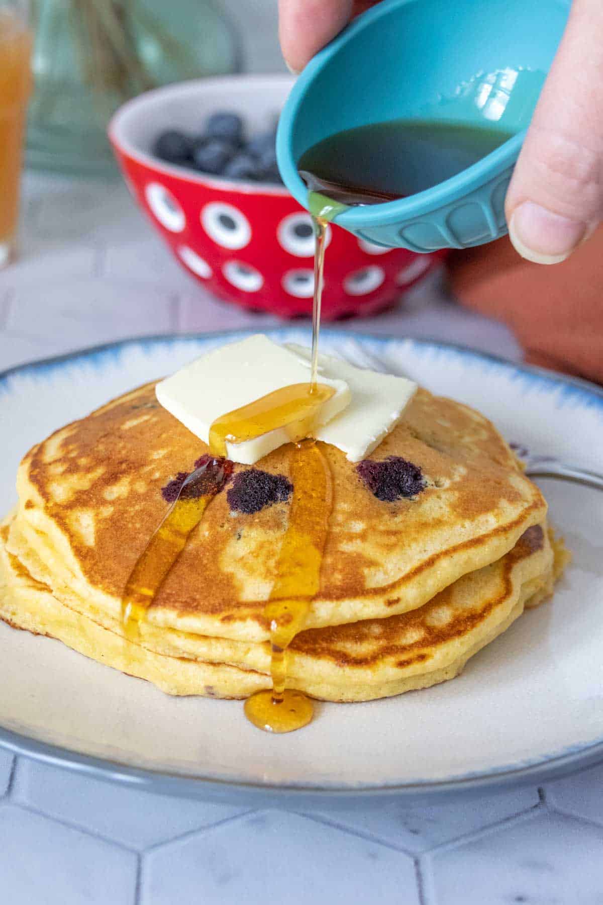 Pouring syrup onto a plate of blueberry pancakes.