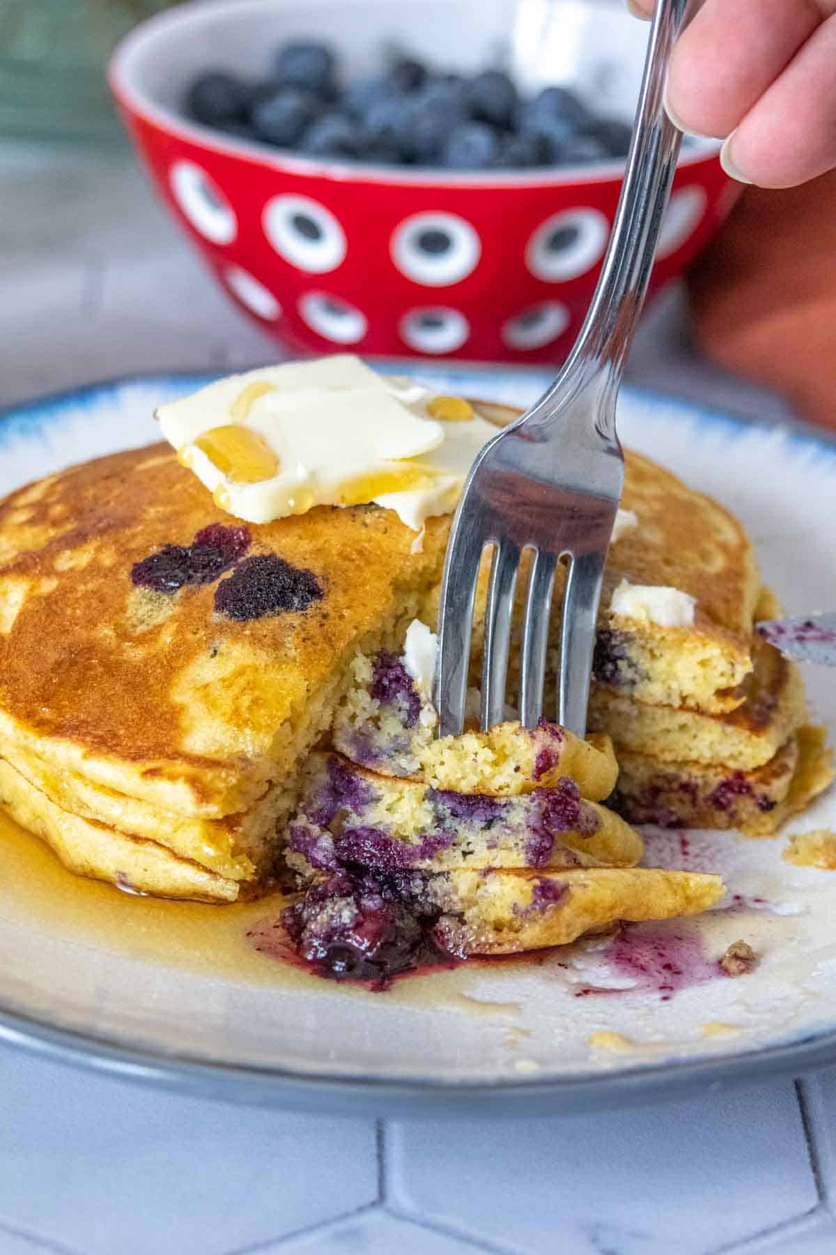 Fork piercing cut pieces of blueberry pancakes.