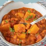 A bowl of hearty butternut squash chili features chunks of tender squash, flavorful beans, and rich tomato sauce, all garnished with fresh herbs.