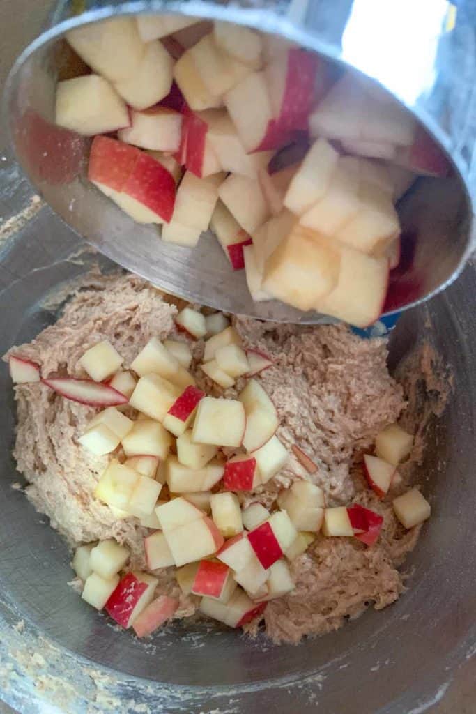 Adding diced apples to muffin batter in a mixing bowl.