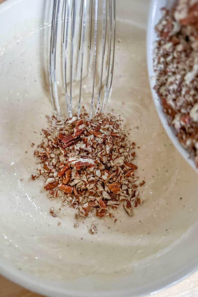 Mixing pecans into pancake batter in a bowl.